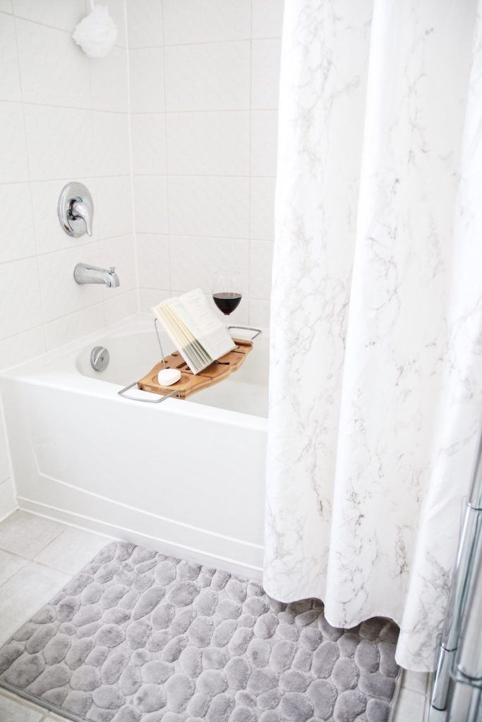 marble shower curtain half open with wooden bathtub caddy across tub