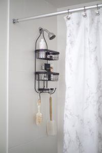 black shower caddy hanging from shower head with bottles on the shelves and brushes hanging